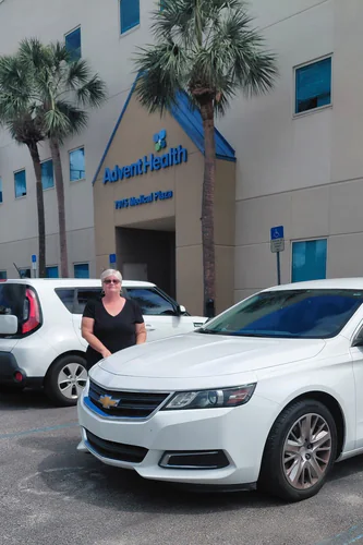 White Comfort Ride Transportation sedan parked outside the AdventHealth medical plaza in East Orlando with a woman standing beside it