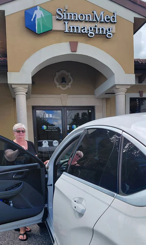 White sedan with its rear door open outside SimonMed Imaging in Orlando as a woman gets ready to ride