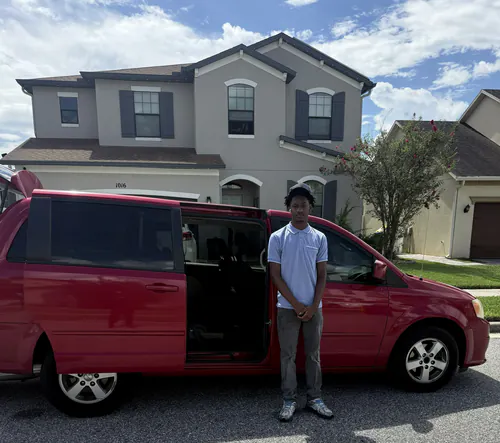 Red minivan with the sliding side door open in front of a two story home in Gainesville